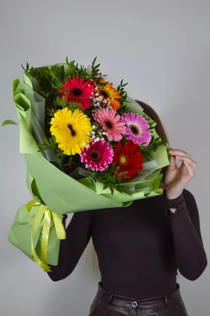 7 разноцветных гербер в зеленой упаковке