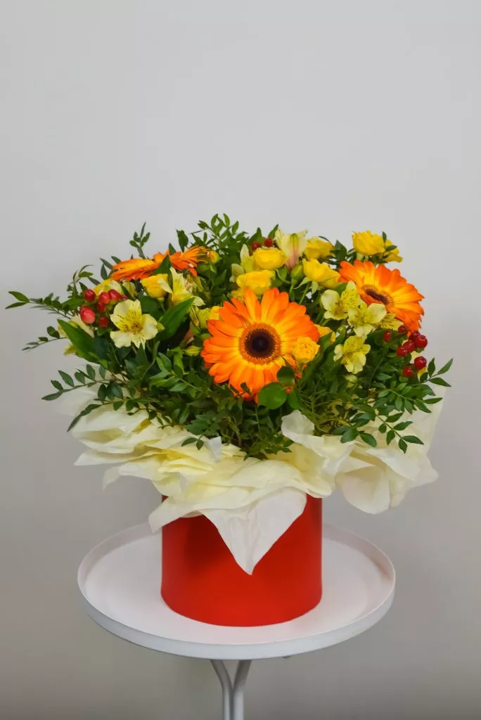 Композиция в шляпной коробке из гербер, гиперикума, альстромерии, кустовой розы и фисташки